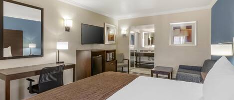 Habitación de hotel con una cama grande, un escritorio con una silla, televisión, microondas, una mesita y un sofá.