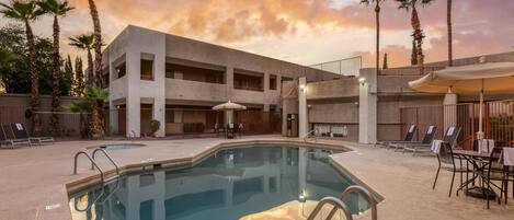 A pool area with a modern building, palm trees, and outdoor seating.
