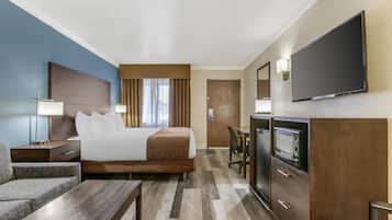 Una habitación de hotel con cama, escritorio, televisor, silla y mesita de noche.