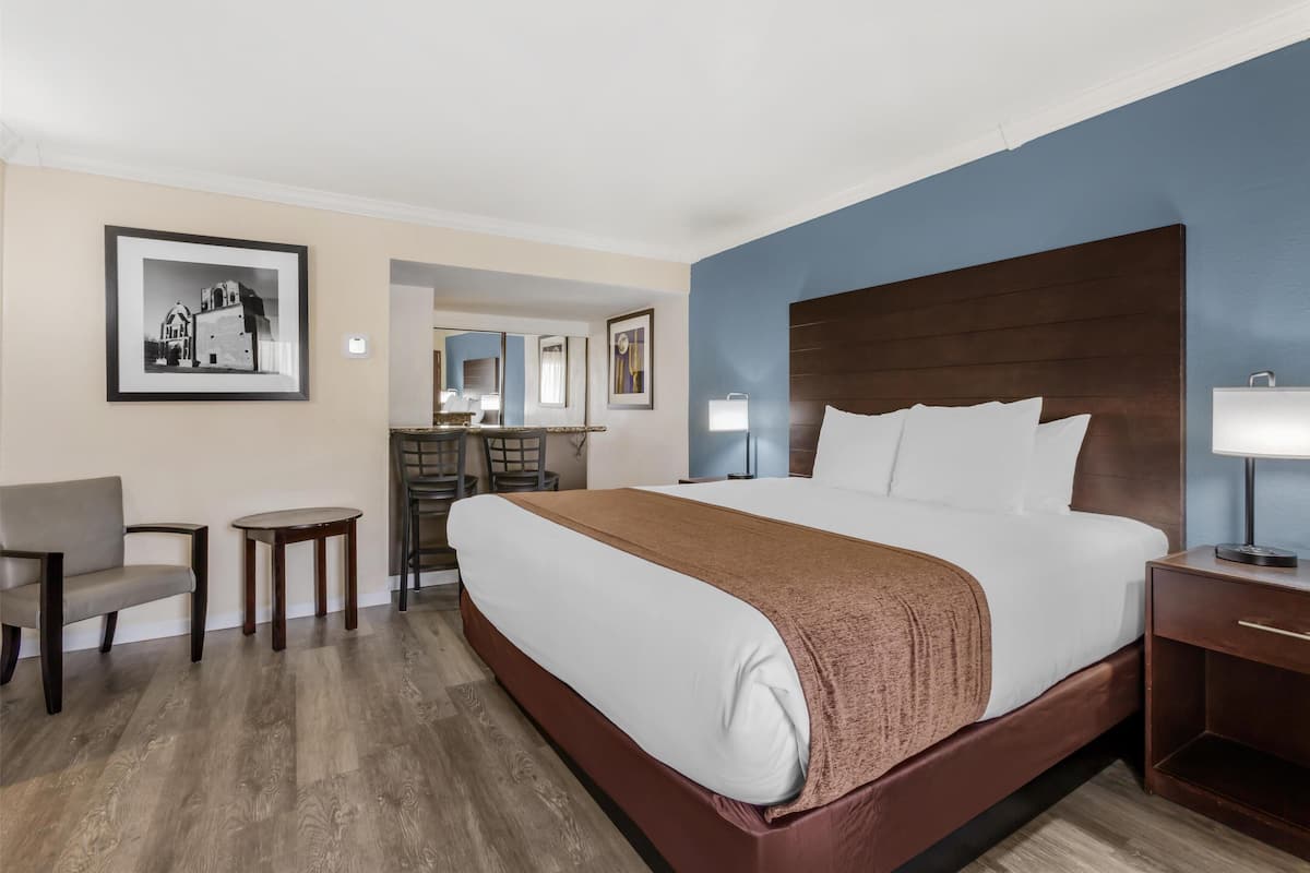 A hotel room with a large bed, a chair, a small table, and artwork on the walls.