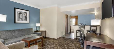 A hotel room with a sofa, armchair, desk, and a television.
