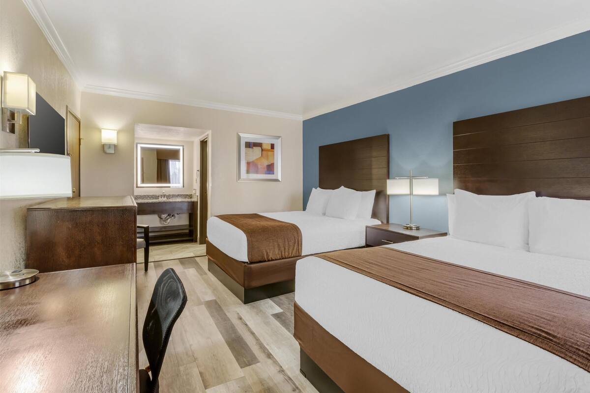 A hotel room with two beds, a desk, a chair, a mirror, and a window.