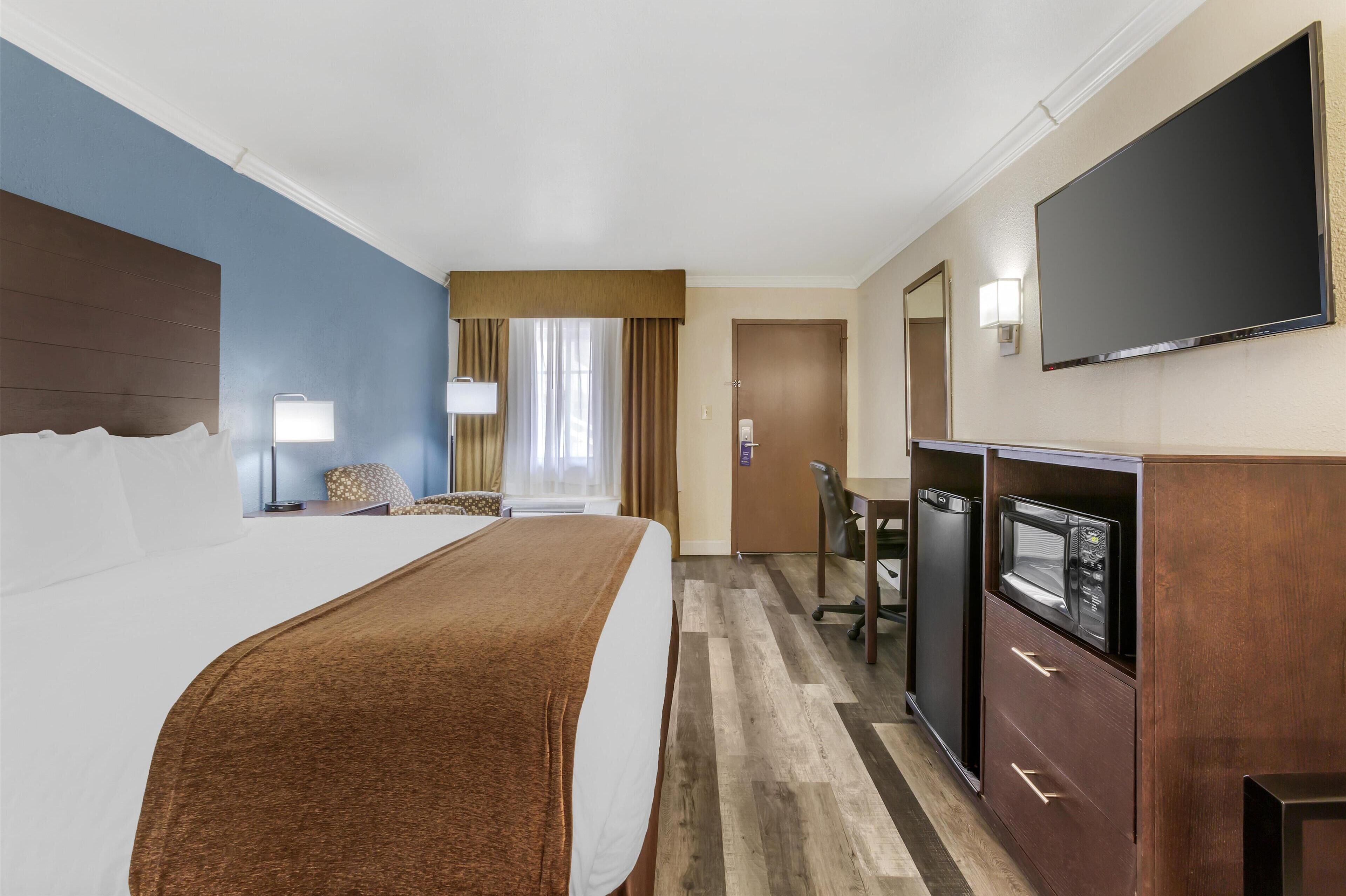 A hotel room with a large bed, a desk with a computer, a television, and a minibar.