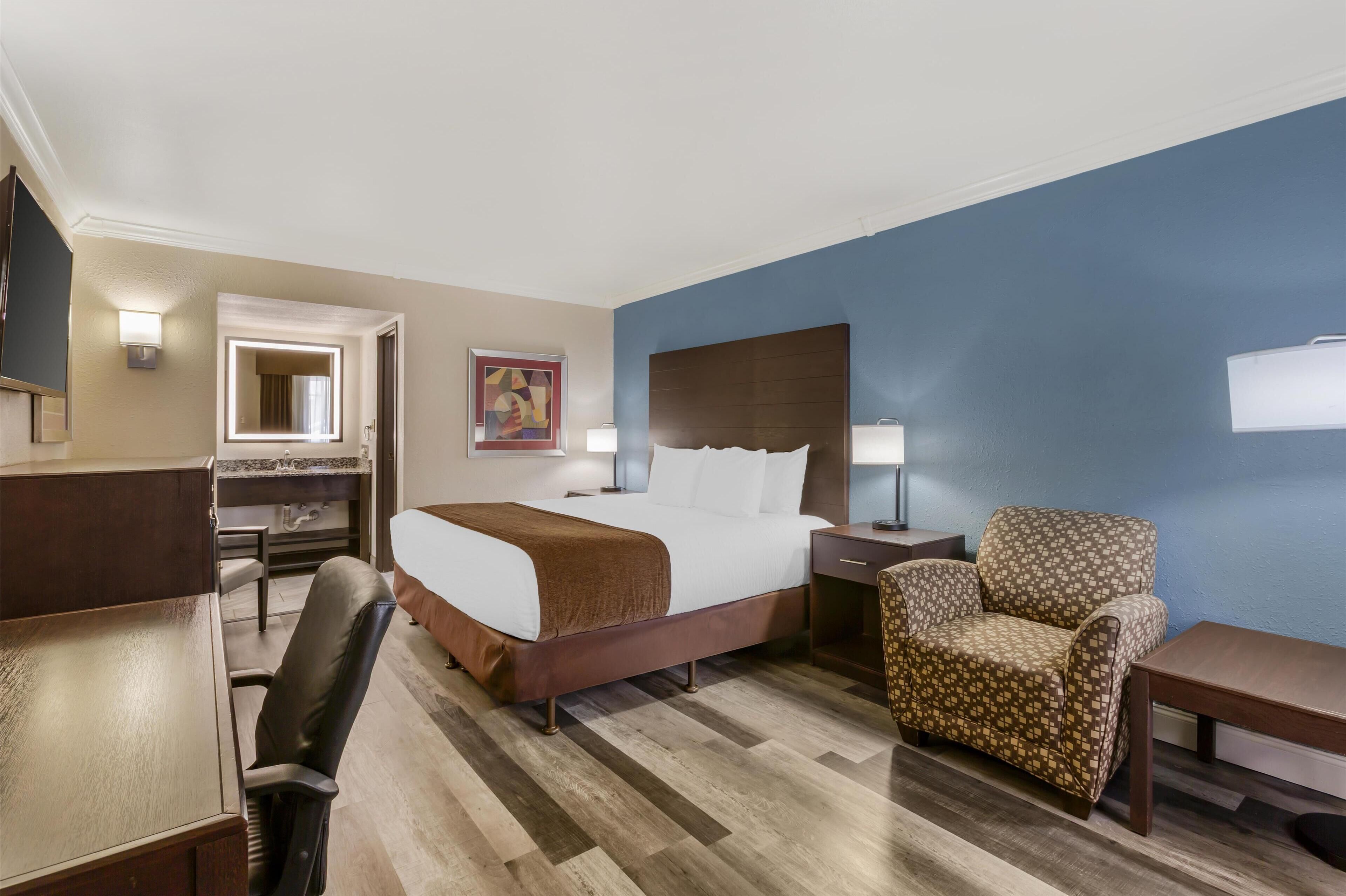 A hotel room with a bed, desk, chair, and a large mirror.