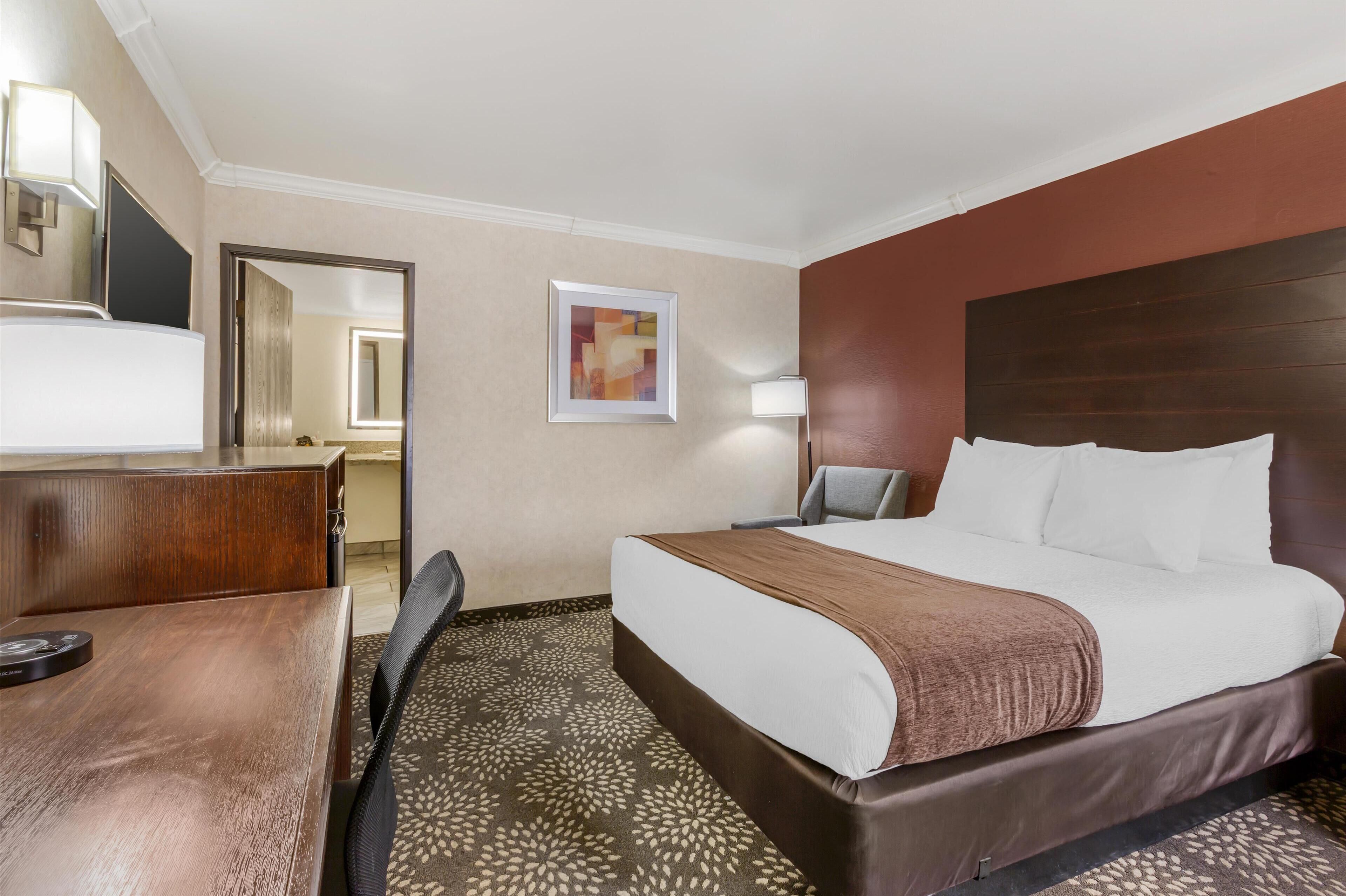 Habitación de hotel con cama, escritorio, silla, lámpara y un cuadro en la pared.