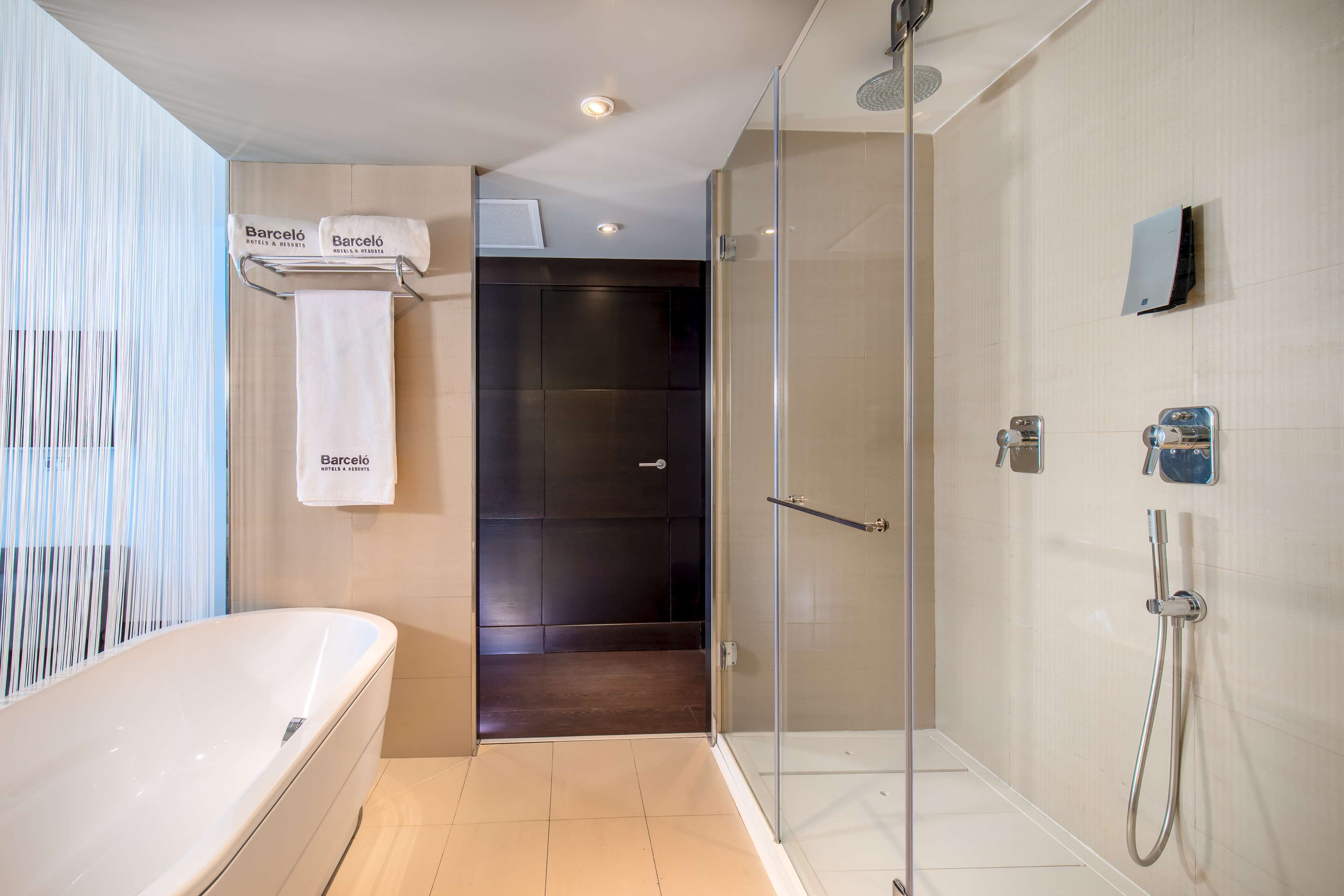 A modern bathroom with a bathtub, a glass-enclosed shower, and a towel rack with branded towels.