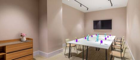 A conference room with a long table, chairs, a whiteboard, and a TV on the wall.