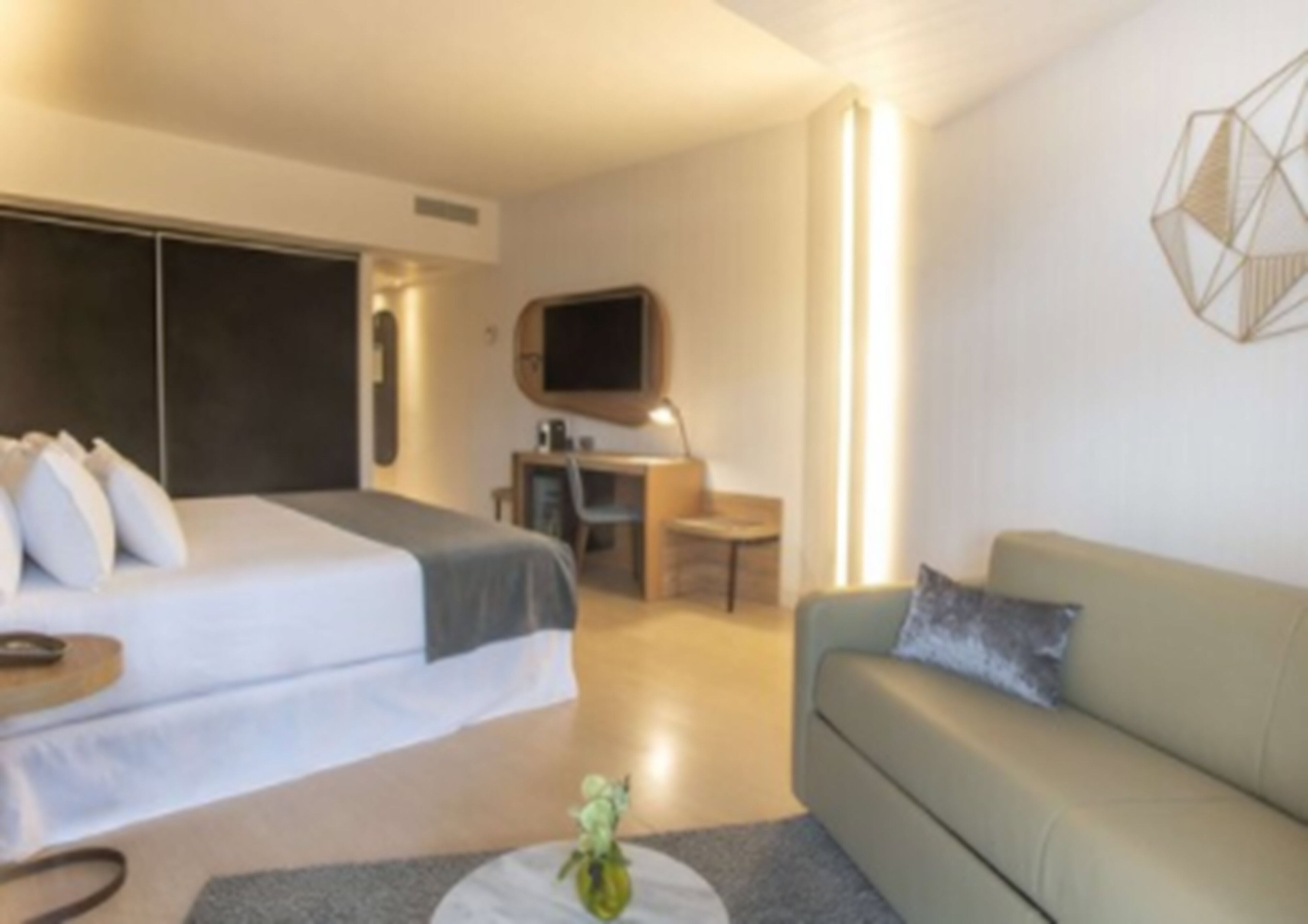 A modern hotel room with a bed, a sofa, a desk, and a TV.