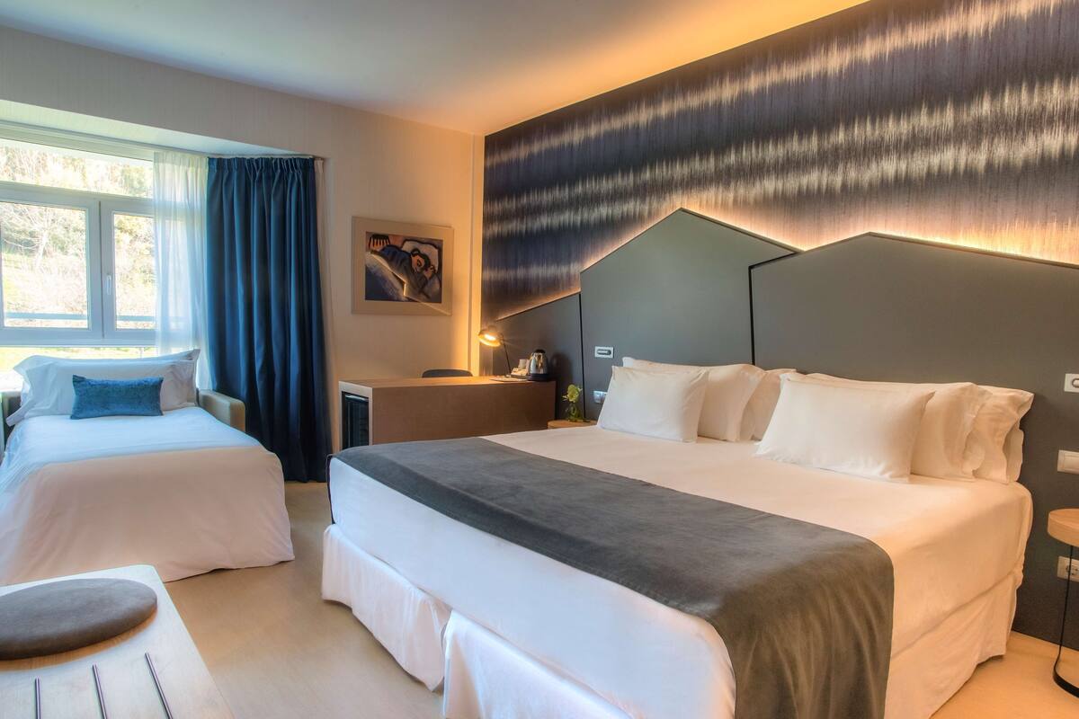 A hotel room with two beds, a desk, and a large window with curtains.