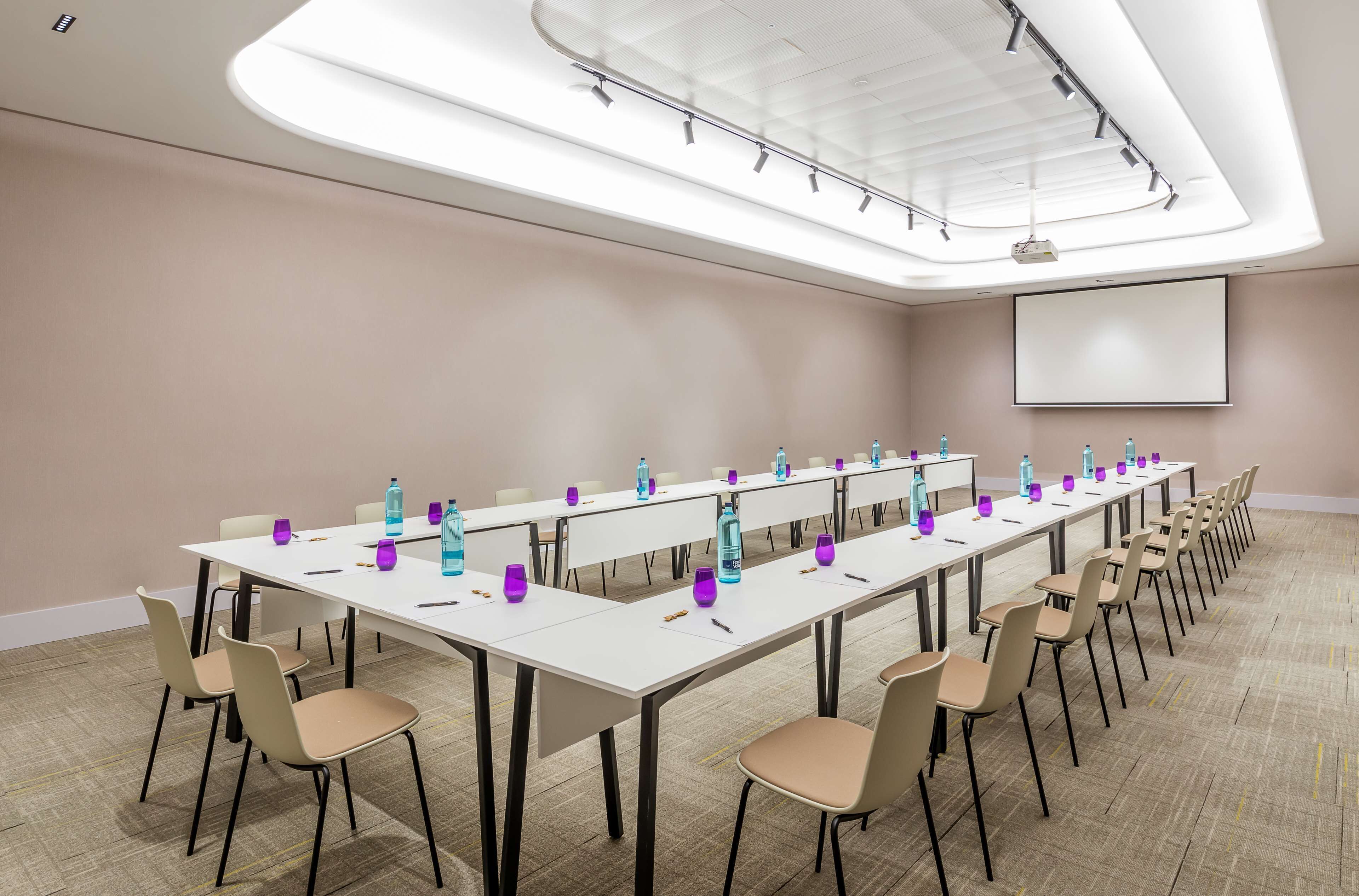 A conference room with a long table, chairs, water bottles, and a projector screen.