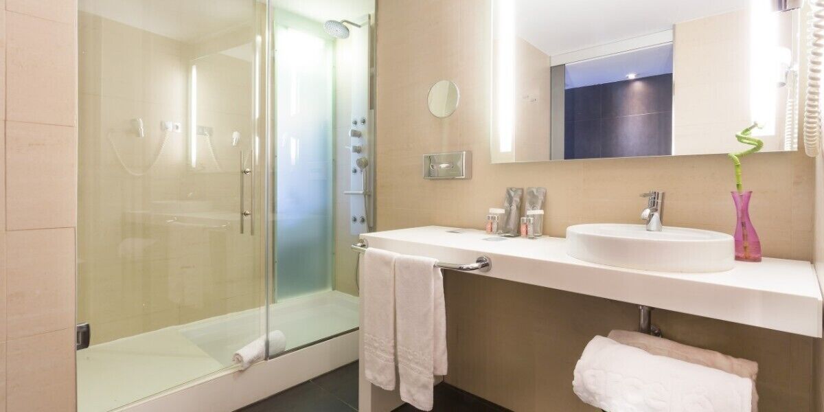 Een moderne badkamer met een douchecabine van glas, een witte wastafel en een spiegel erboven.