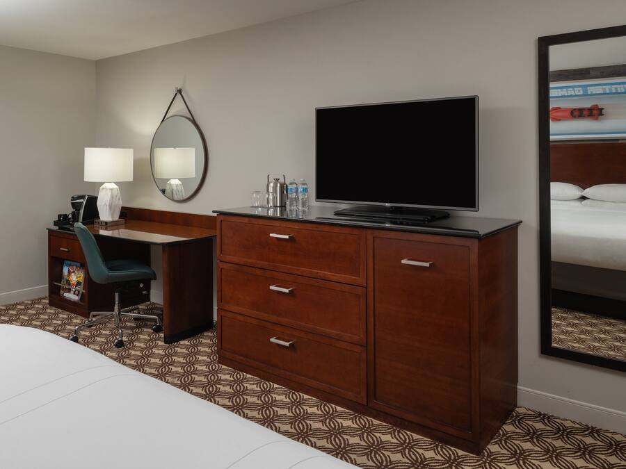 Een hotelkamer met een bed, een bureau met stoel, een televisie, een spiegel en een kledingkast.
