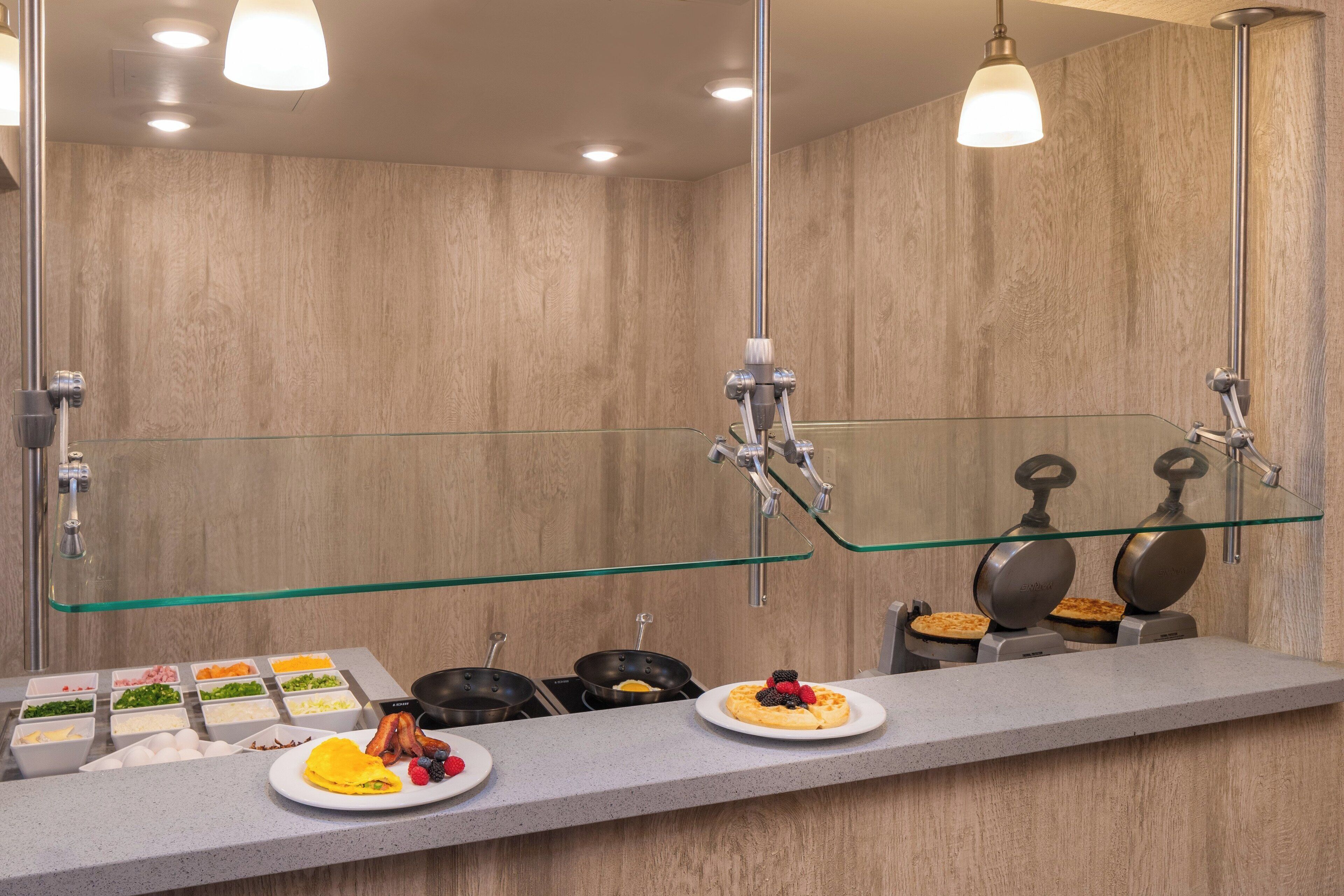 Une salle de bain moderne dotée d’une douche à parois de verre, d’un meuble-lavabo avec miroir et d’un bar pour prendre le petit-déjeuner, où sont disposés divers aliments.