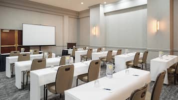 Un salón de conferencias con varias mesas, sillas, una pantalla de proyector y un atril.