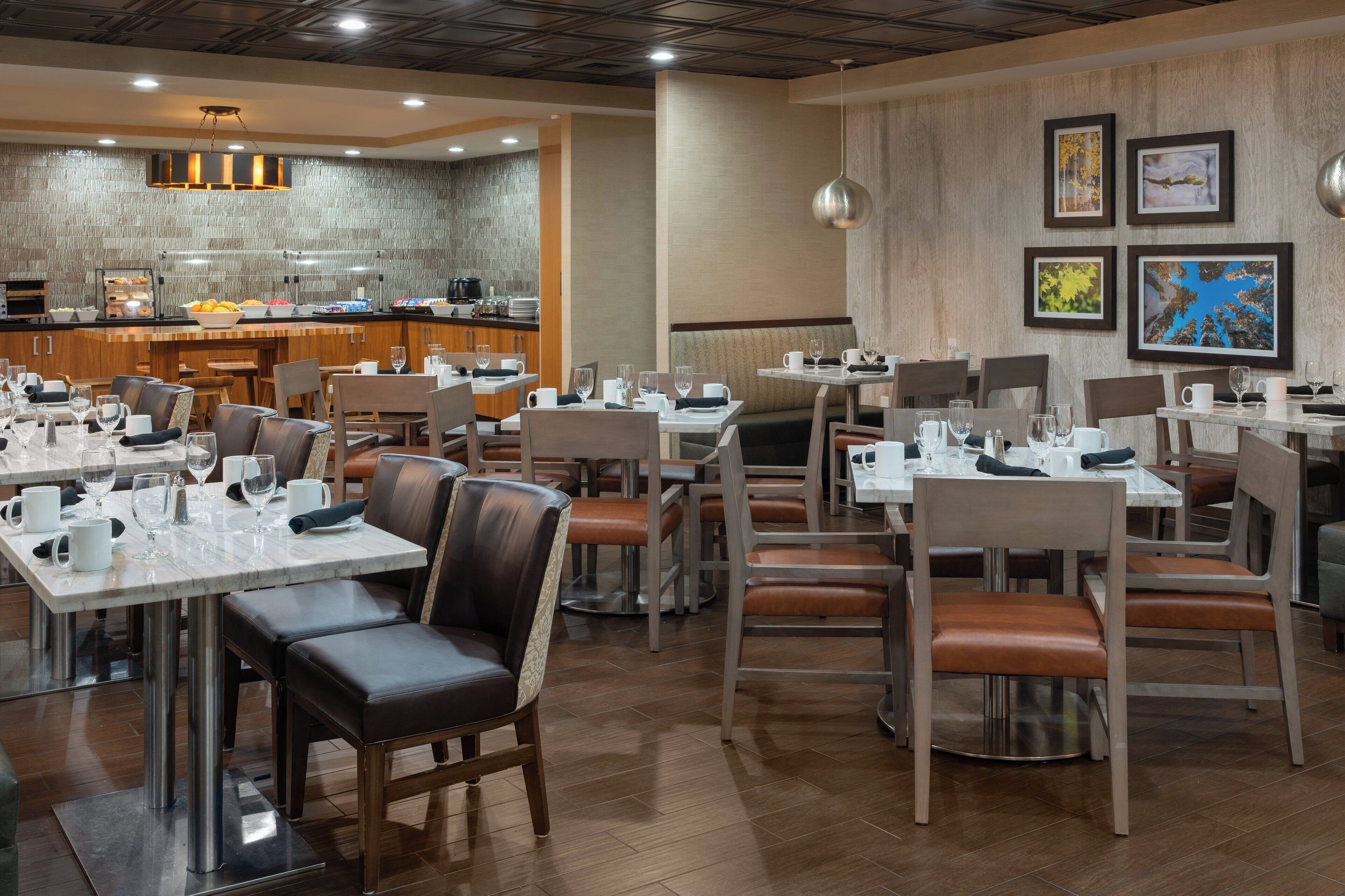 A modern restaurant with multiple dining tables and booths, a kitchen area, and framed artwork on the walls.