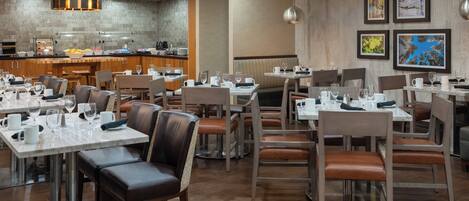 Un restaurant moderne doté de nombreuses tables et de coins repas, d’un espace cuisine et d’œuvres d’art encadrées qui ornent les murs.