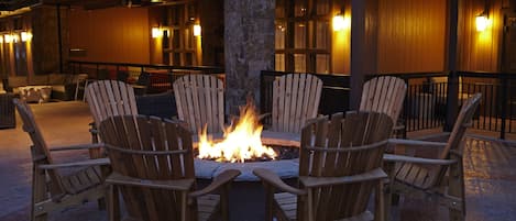 A fire pit surrounded by wooden chairs in an outdoor seating area with stone pillars and wooden walls.