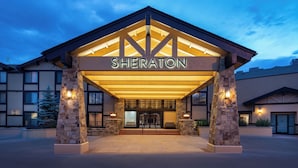 Der Eingang eines Sheraton Hotels mit einer Steinfassade, großen Glasüren und einem überdachten Zugang.