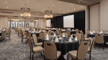 A large conference room with round tables, beige chairs, and chandeliers.