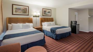 A hotel room with two beds, a desk, a chair, a refrigerator, and two paintings on the wall.