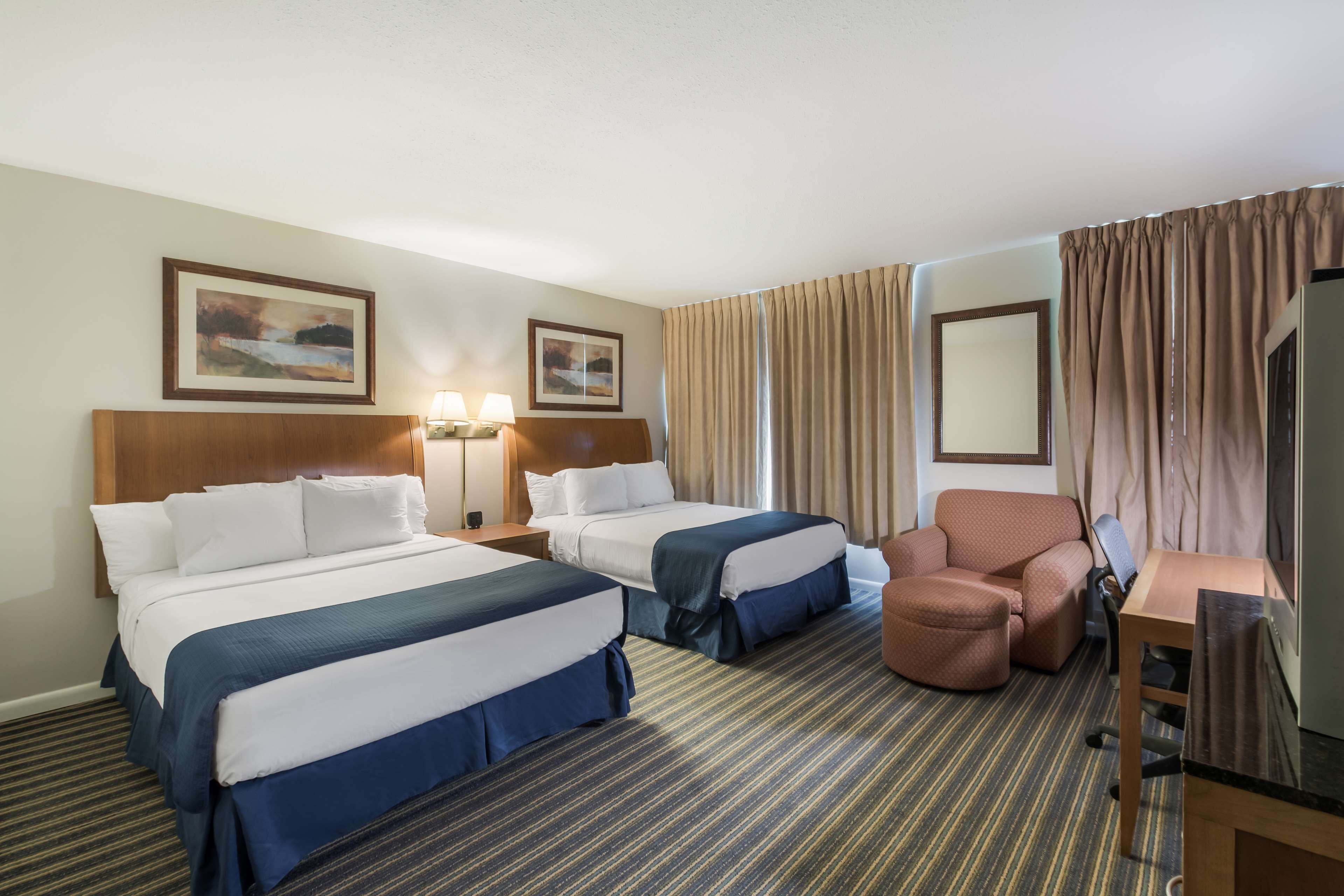 A hotel room with two beds, a desk, a chair, and a TV.