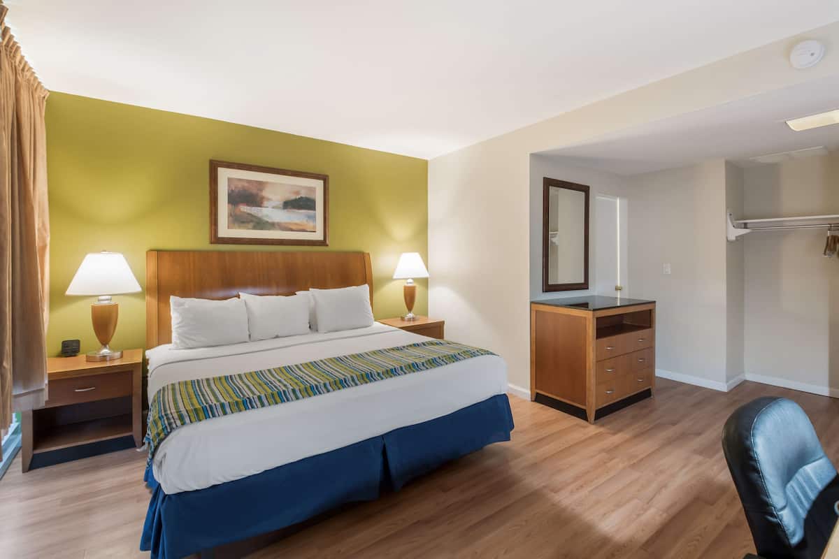 A hotel room with a bed, two bedside tables with lamps, a dresser, a mirror, and a chair.