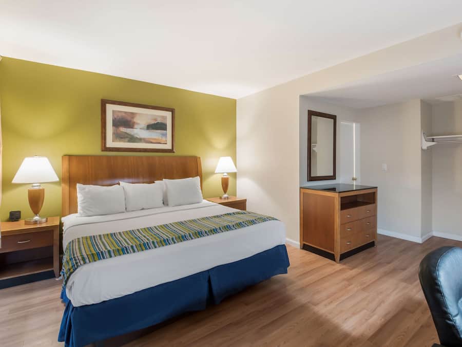 Hotellihuone, jossa on sänky, kaksi yöpöytää valaisimineen, lipasto, peili ja tuoli.