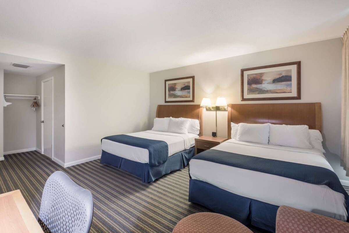 A hotel room with two beds, a desk, a chair, and two wall-mounted lamps.
