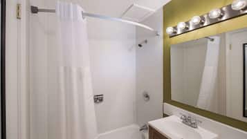 Une salle de bain avec une douche, un lavabo, un miroir avec éclairage et un porte-serviettes.