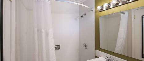 A bathroom with a shower, a sink, a mirror with lights, and a towel rack.