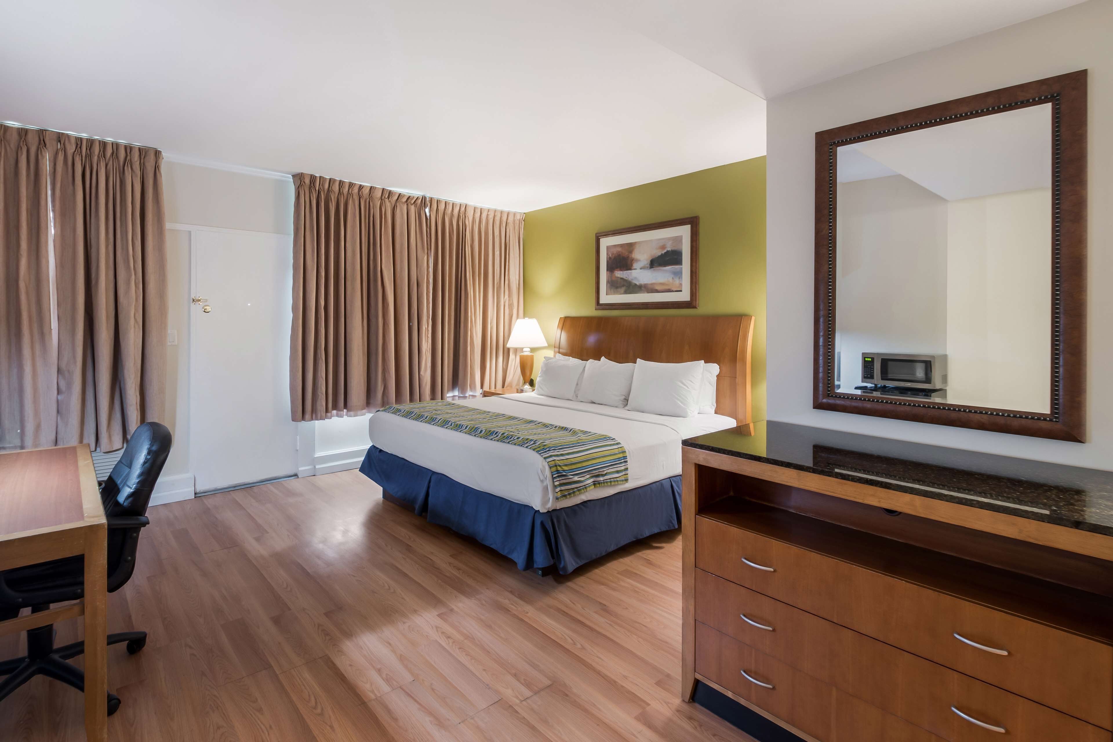 Una habitación de hotel con cama, escritorio, silla, cómoda y un espejo grande.