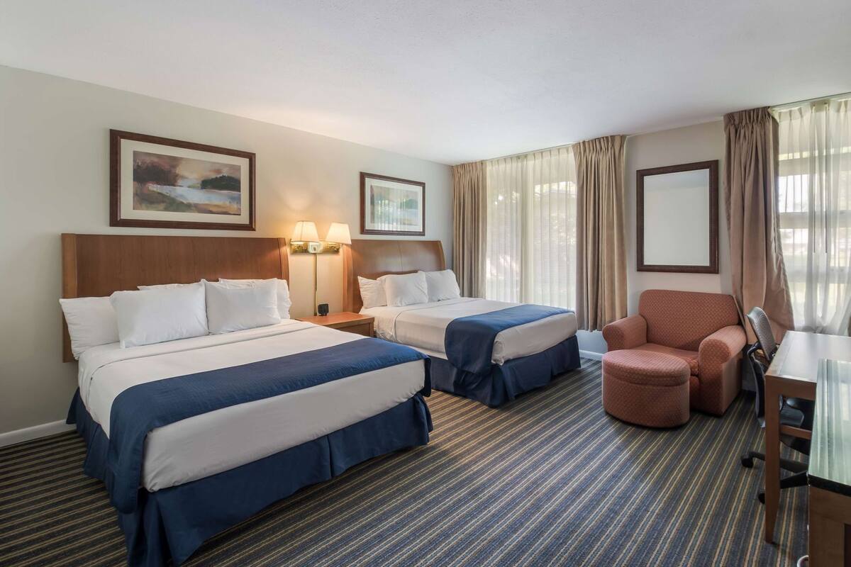 A hotel room with two beds, a desk, a chair, and a large window with curtains.