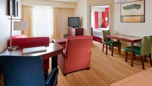 A hotel room with a red sofa, a dining table with chairs, a TV on a cabinet, and a painting on the wall. - Residence Inn By Marriott Peoria (Peoria)