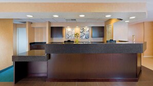 A reception area with a dark wood reception desk, a vase with green flowers, and abstract wall art. - Residence Inn By Marriott Peoria (Peoria)
