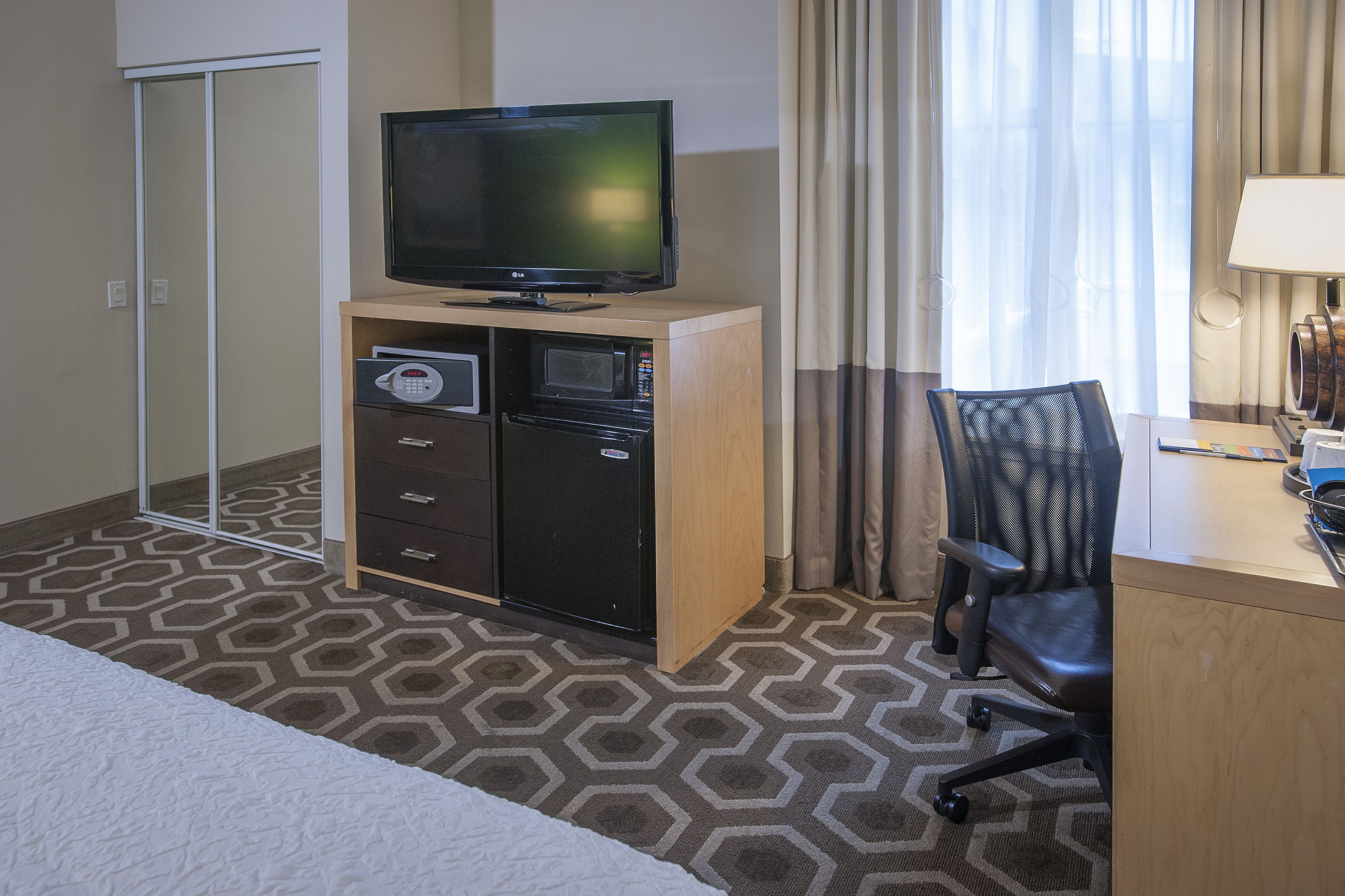 A hotel room with a bed, a desk with a computer, a television on a cabinet, a microwave, and a telephone.