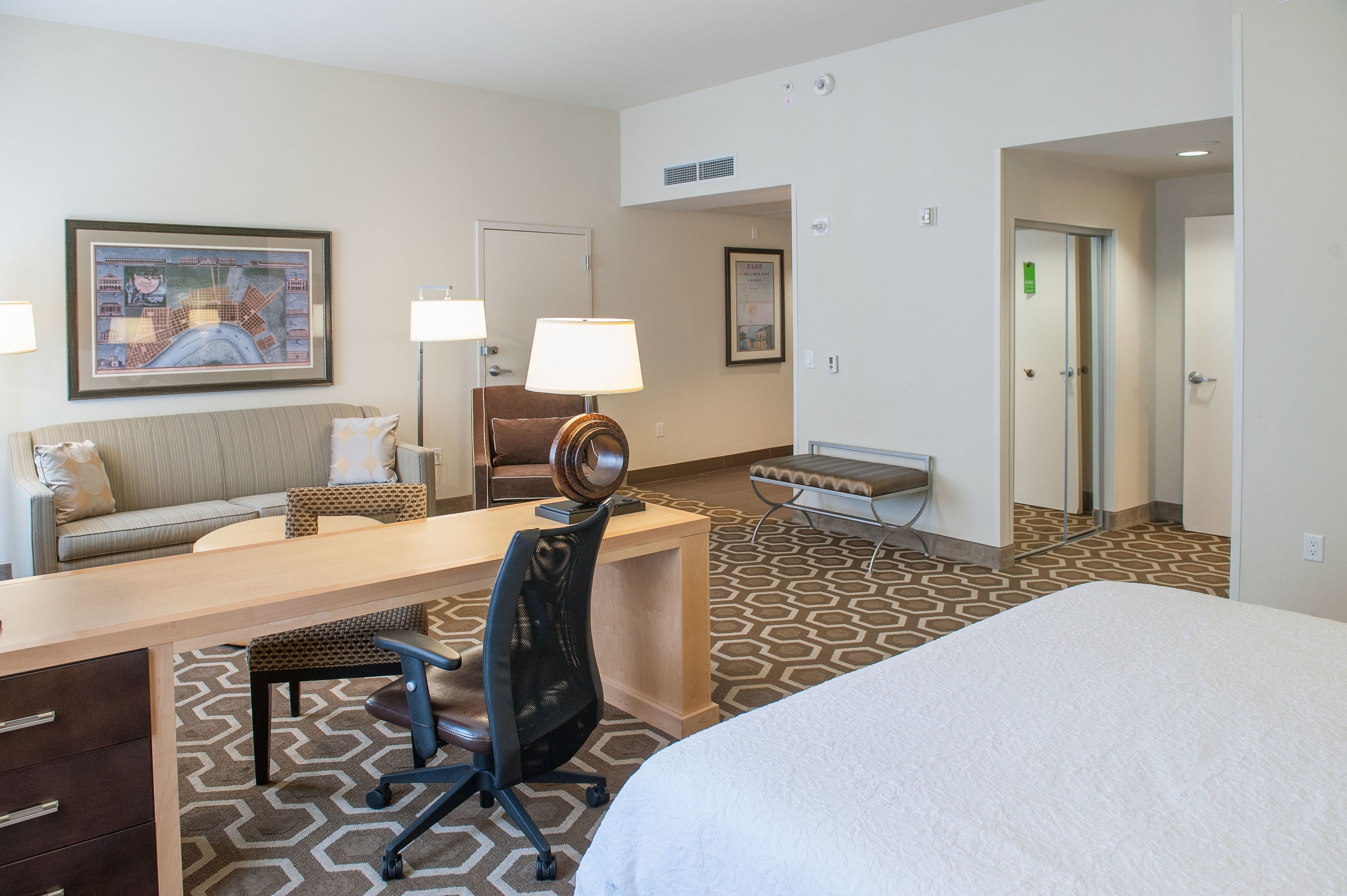 A hotel room with a bed, a desk, a chair, a sofa, a lamp, and a framed picture on the wall.