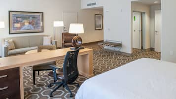A hotel room with a bed, a desk, a chair, a sofa, a lamp, and a framed picture on the wall.