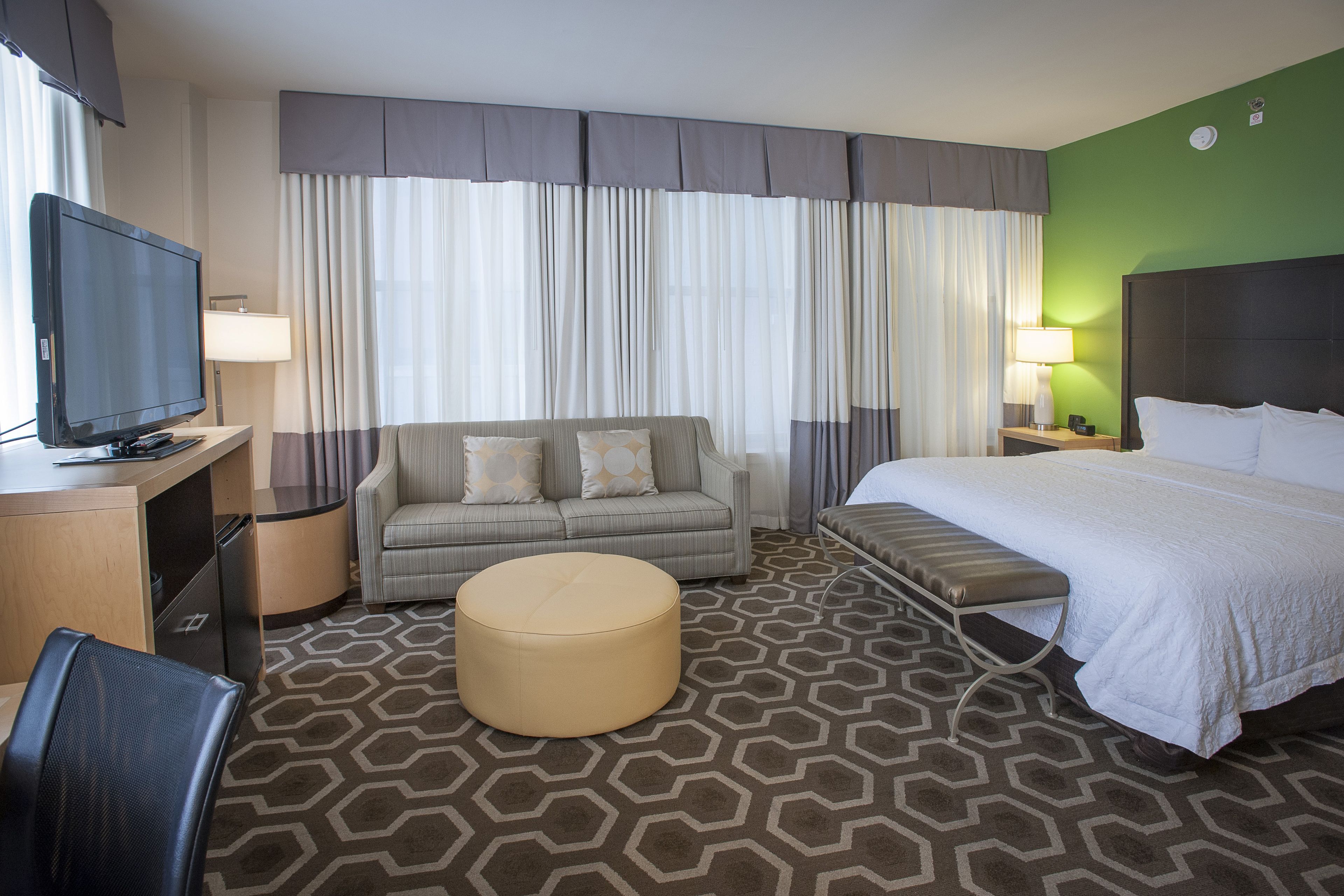 A hotel room with a bed, a sofa, a TV, a desk, and a bathroom.