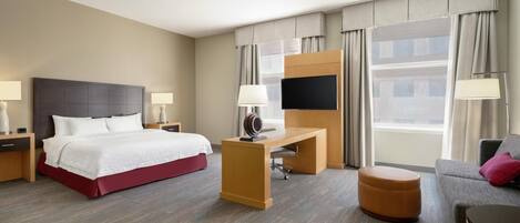 Ein Hotelzimmer mit Bett, Schreibtisch, Fernseher, Sofa und Hocker.