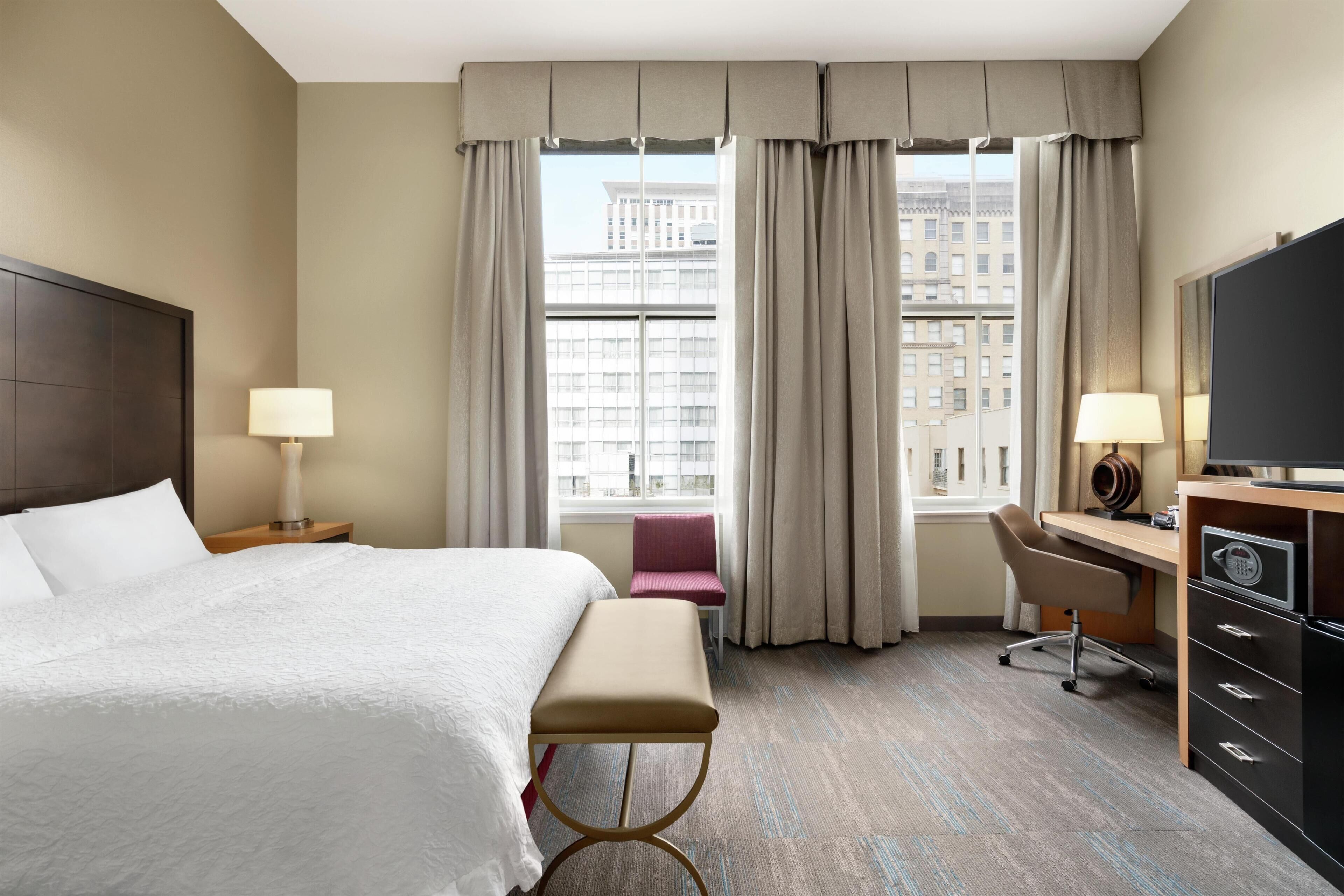 Une chambre d’hôtel équipée d’un lit, d’un bureau, d’une chaise, d’une télévision et offrant une vue sur la ville.