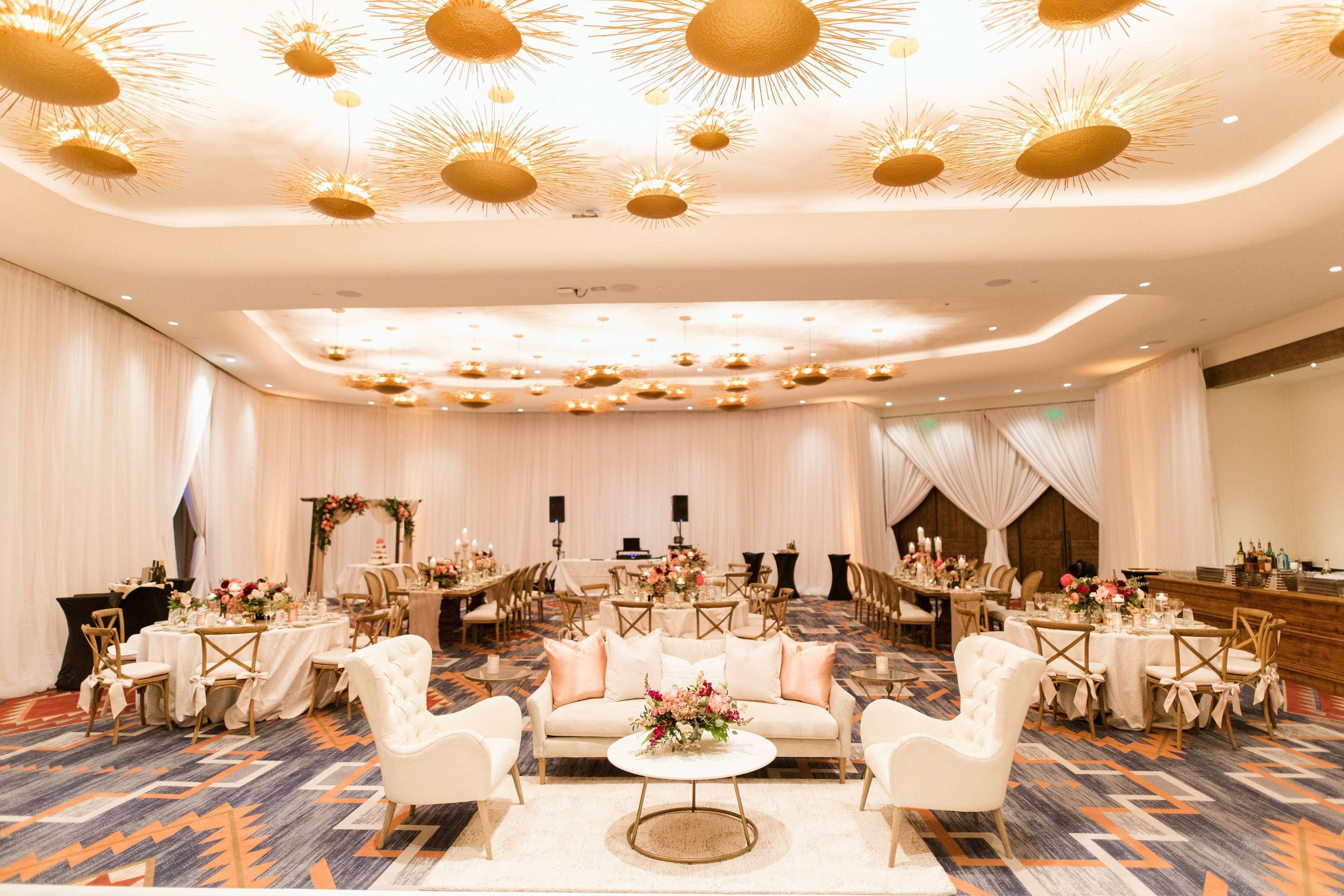 A spacious banquet hall with round tables, white chairs, and a central sofa.