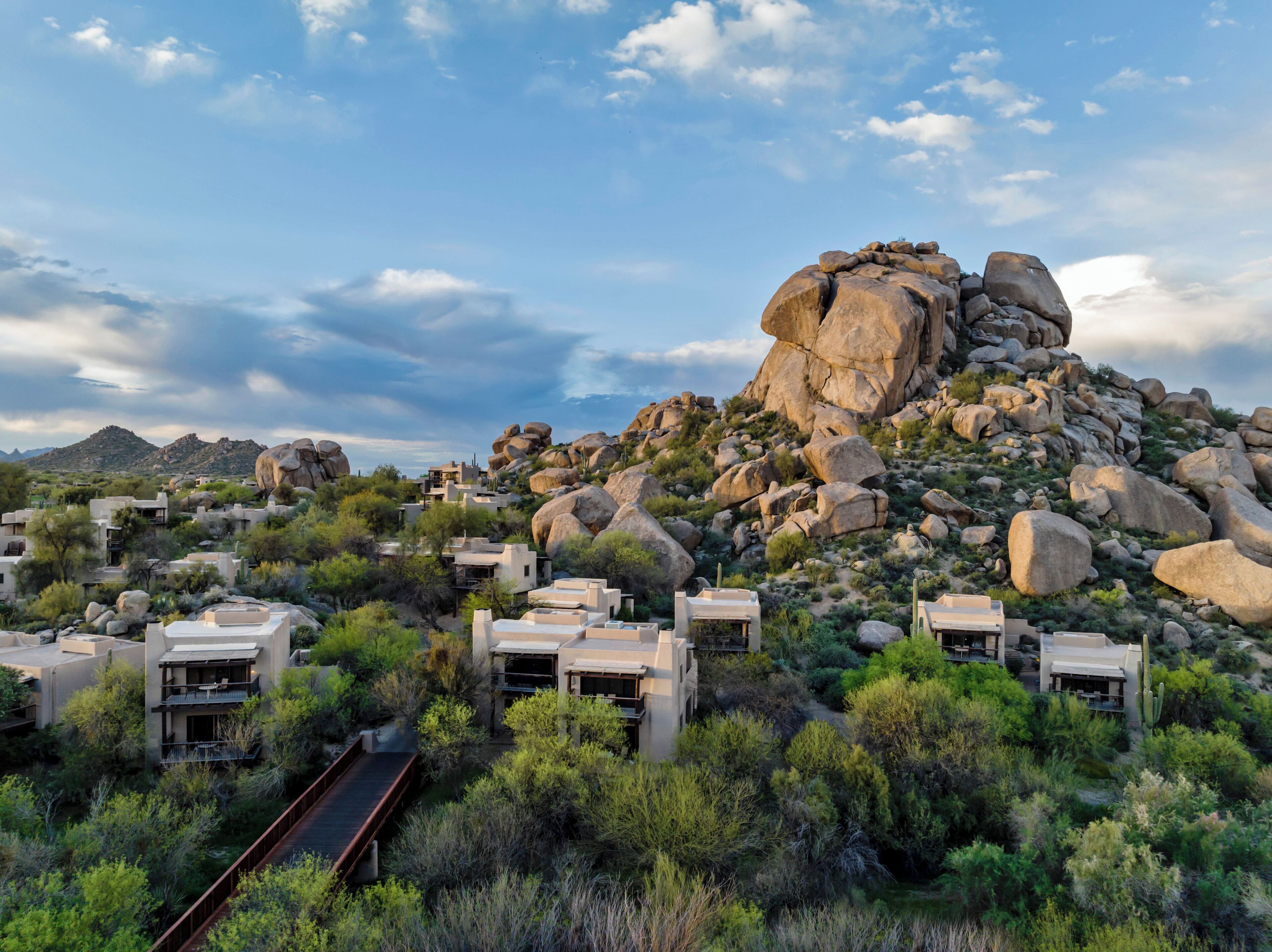 A desert resort with modern villas, a rocky hill, and a wooden bridge.