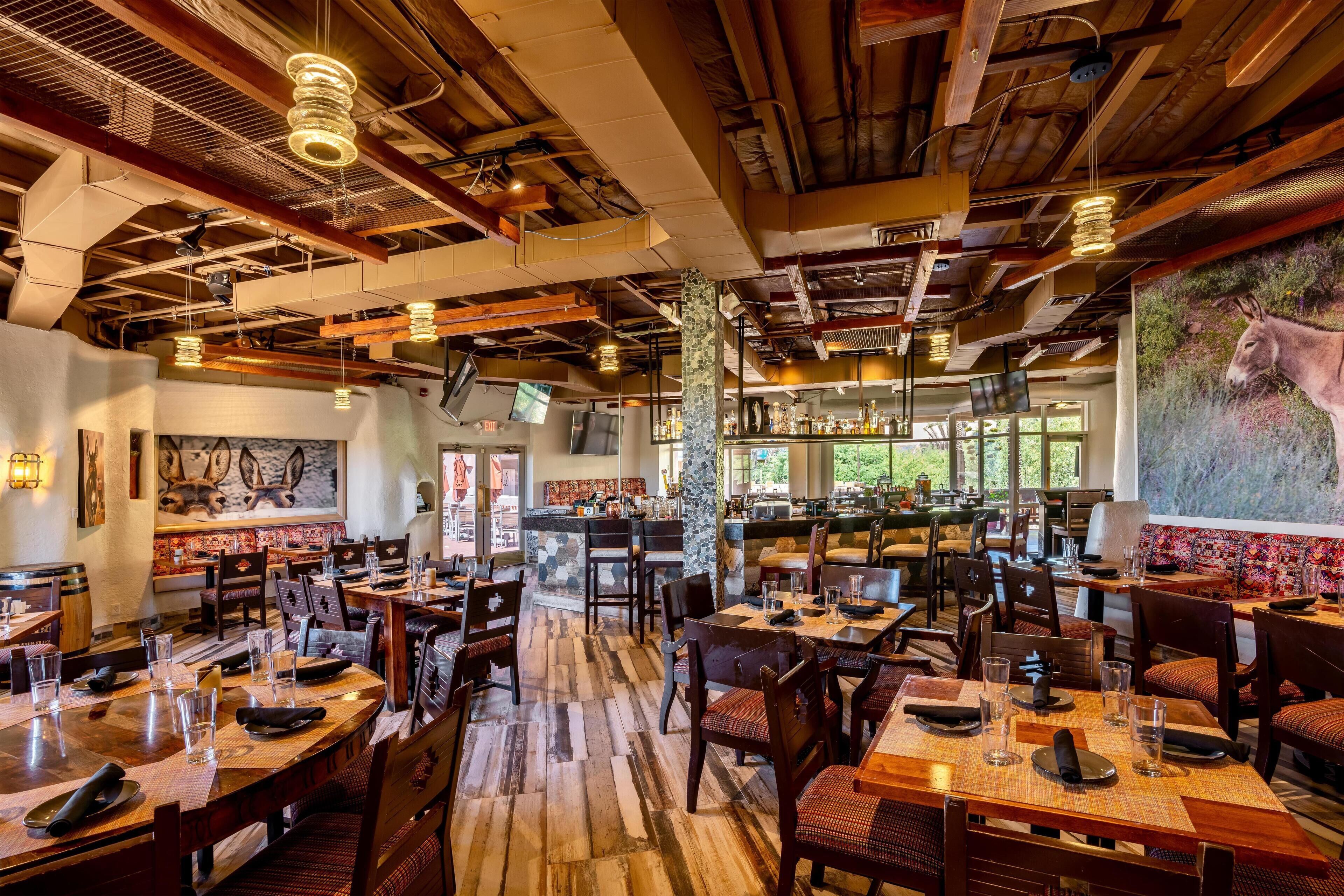 A restaurant with wooden tables and chairs, a bar area, and a mural of a donkey.