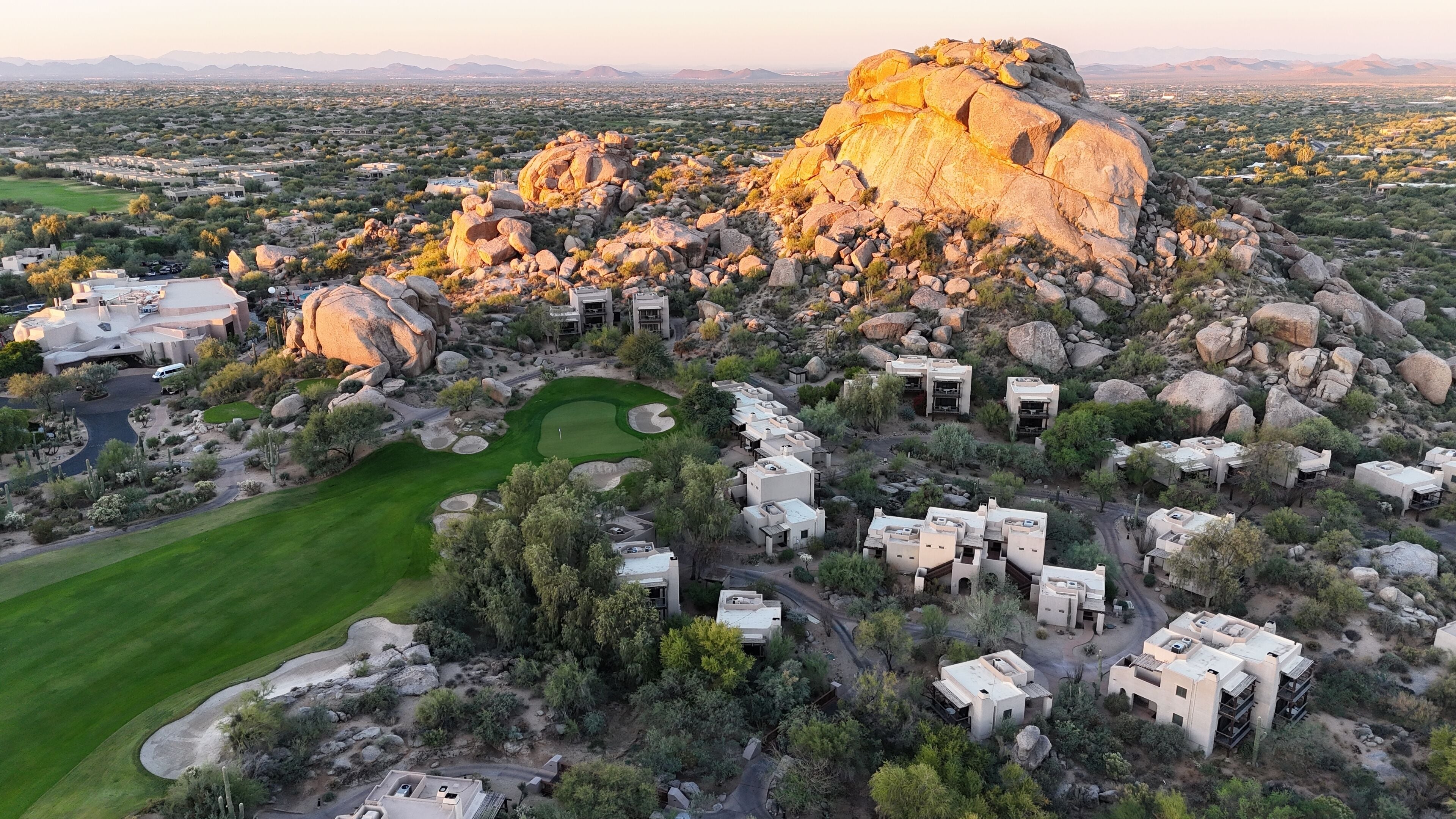 An aerial view of a resort with multiple buildings, a golf course, and large rock formations.