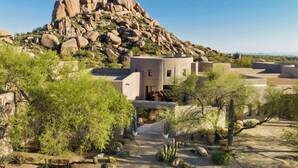 A desert landscape with a large rock formation, a building with a flat roof, and a paved walkway. - Boulders Resort & Spa Scottsdale, Curio Collection by Hilton (Scottsdale)