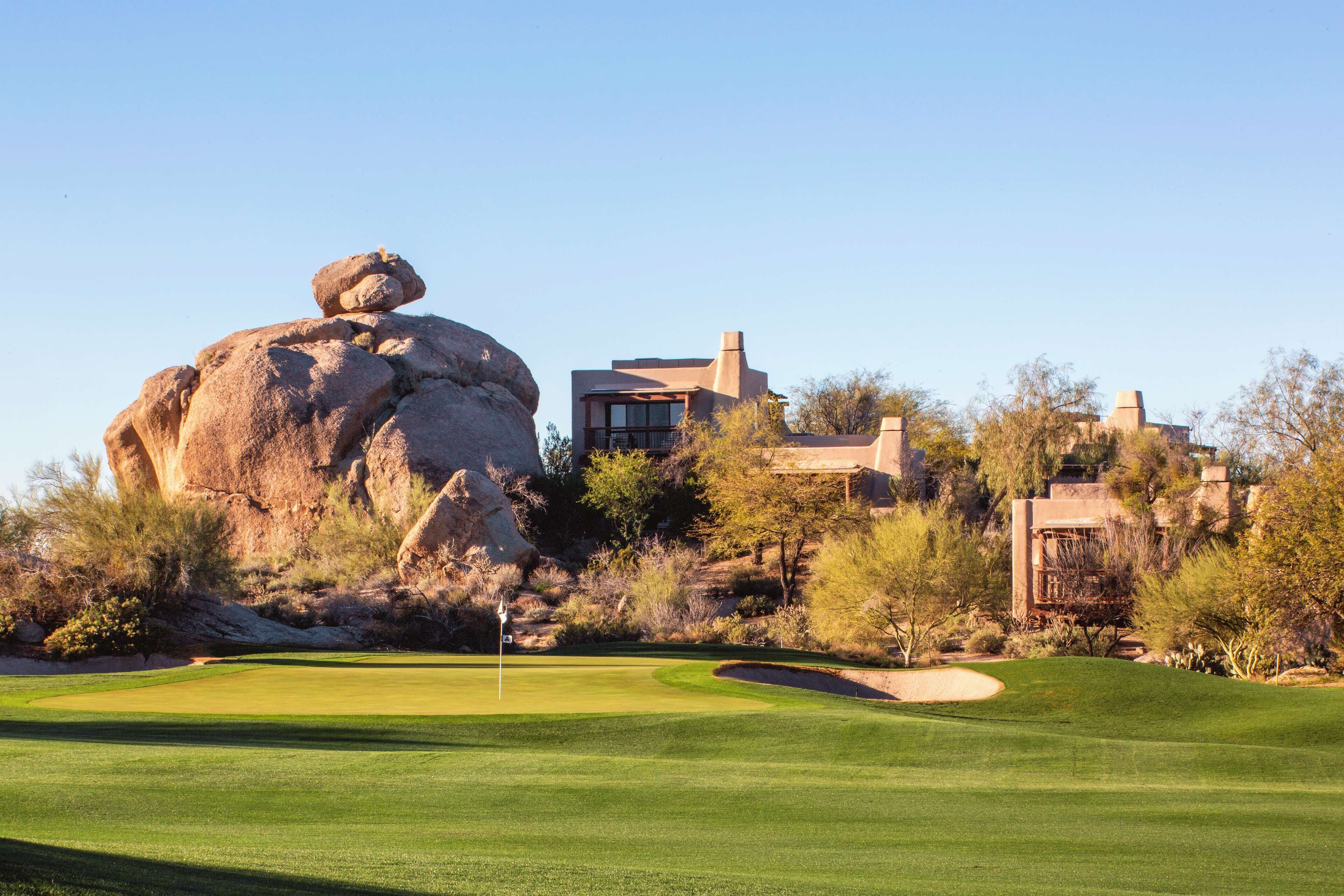 A golf course with a large rock formation, a modern building, and a clear sky.