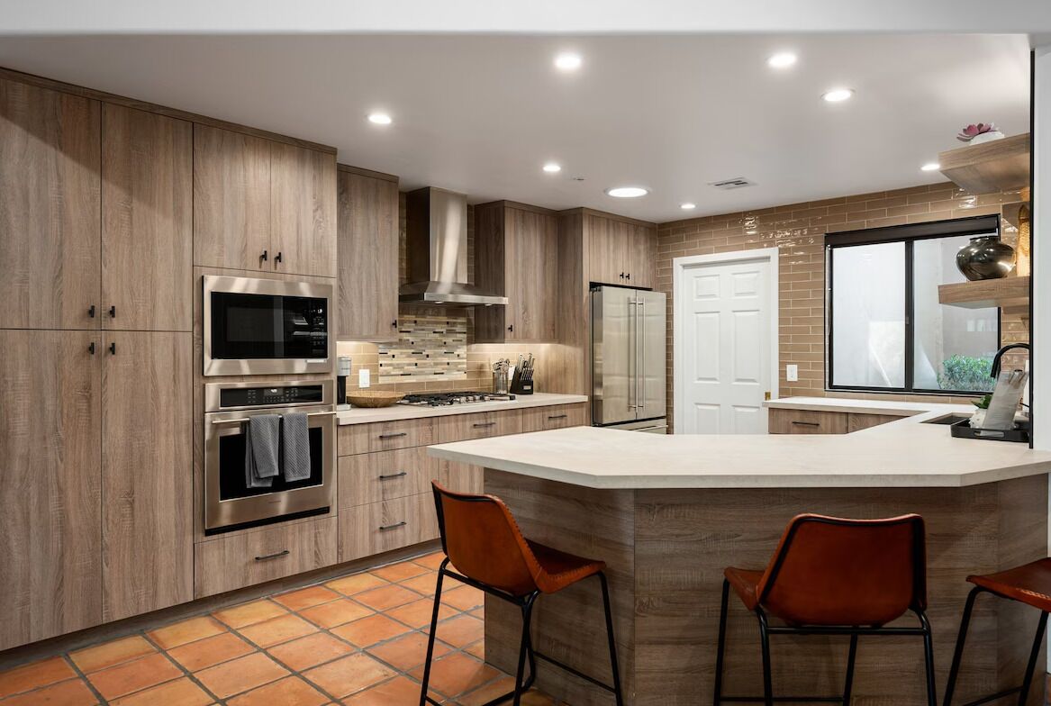 A modern kitchen with wooden cabinets, stainless steel appliances, and a large island with bar stools.