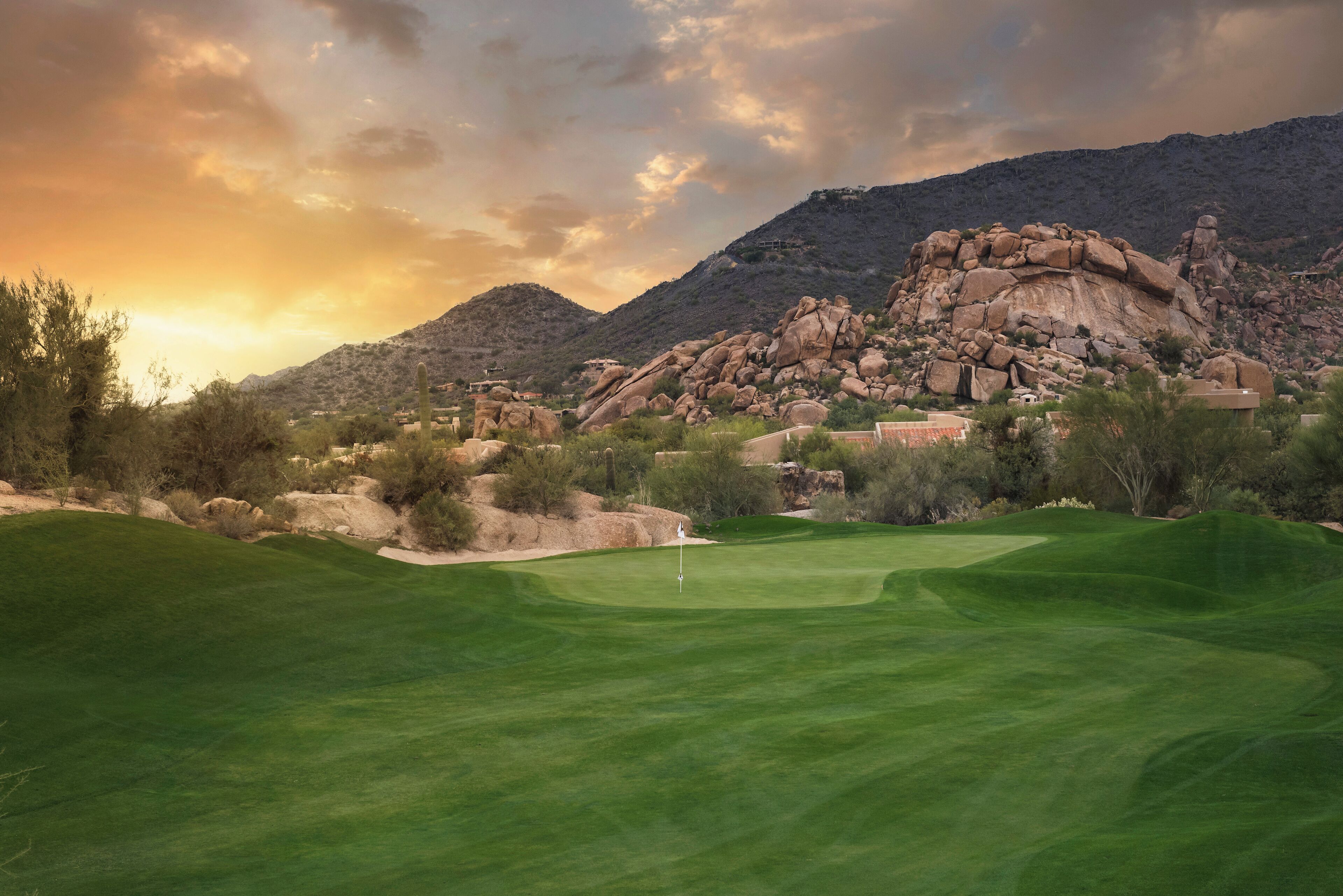 A golf course with a flagstick, surrounded by rocky terrain and sparse vegetation.