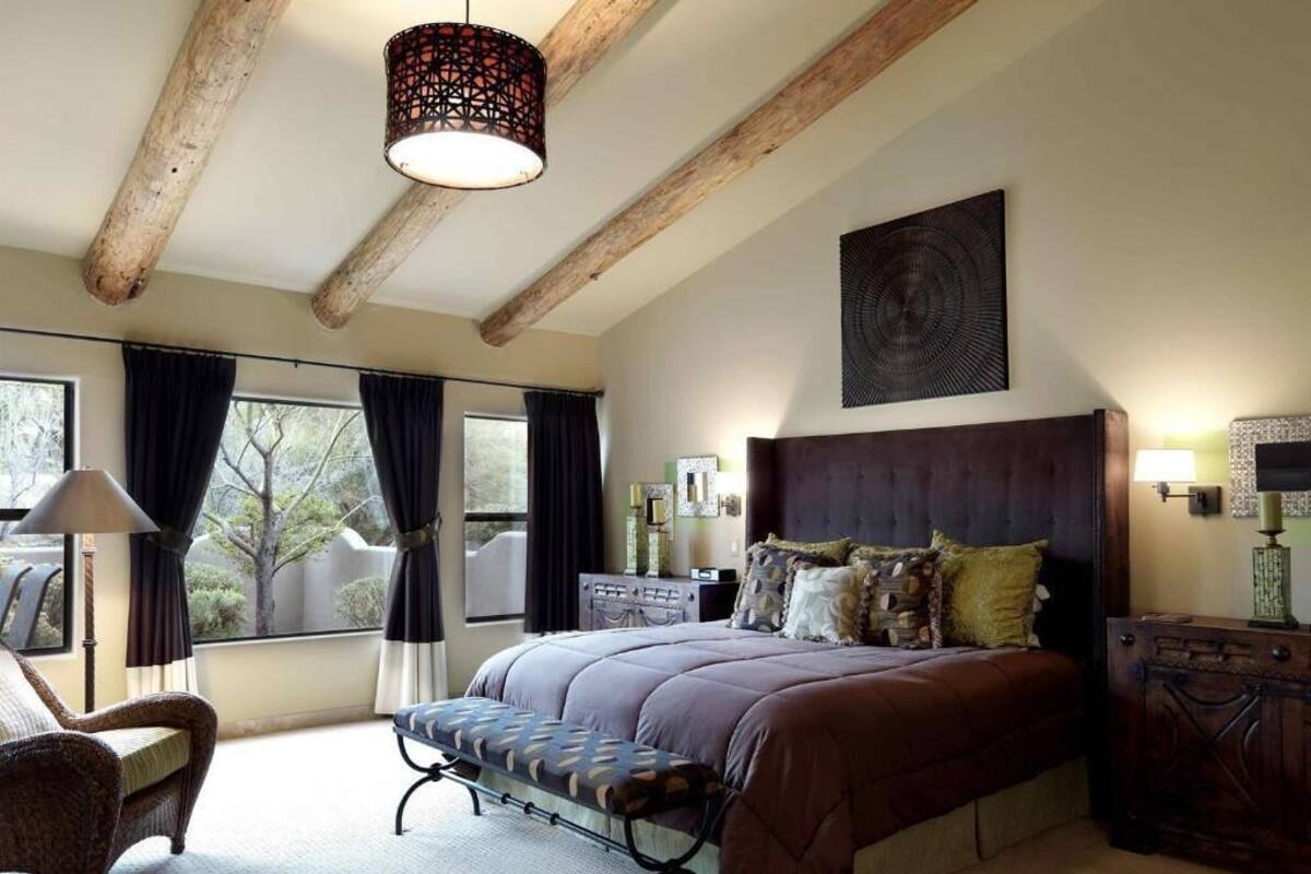 Une chambre à coucher avec un grand lit, un banc, une chaise, un bureau et une fenêtre avec des rideaux.