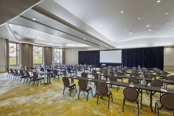 A conference room with rows of tables and chairs, a large screen, and a projector. - Boulders Resort & Spa Scottsdale, Curio Collection by Hilton (Scottsdale)